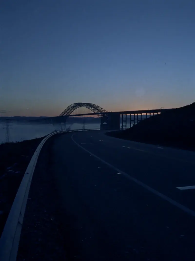 An empty highway at dawn curving toward a river bridge crossing
