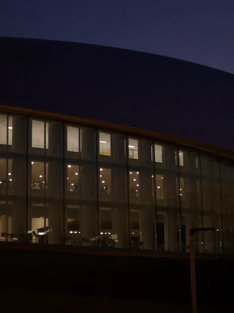 A modern arena glass facade lit from within at dusk
