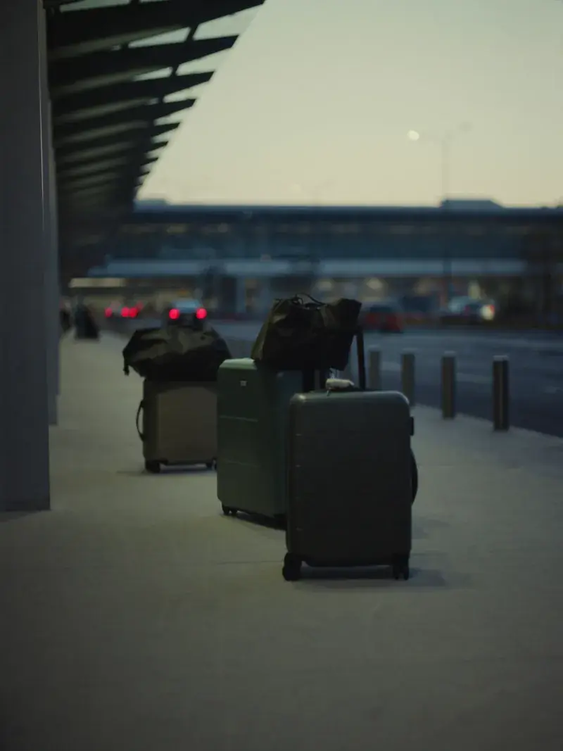 Suitcases and travel bags lined up on an airport terminal curb at dawn