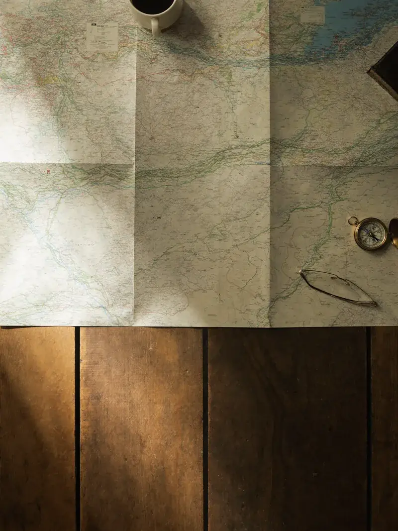 A folded paper road map, compass and coffee cup on a wooden table